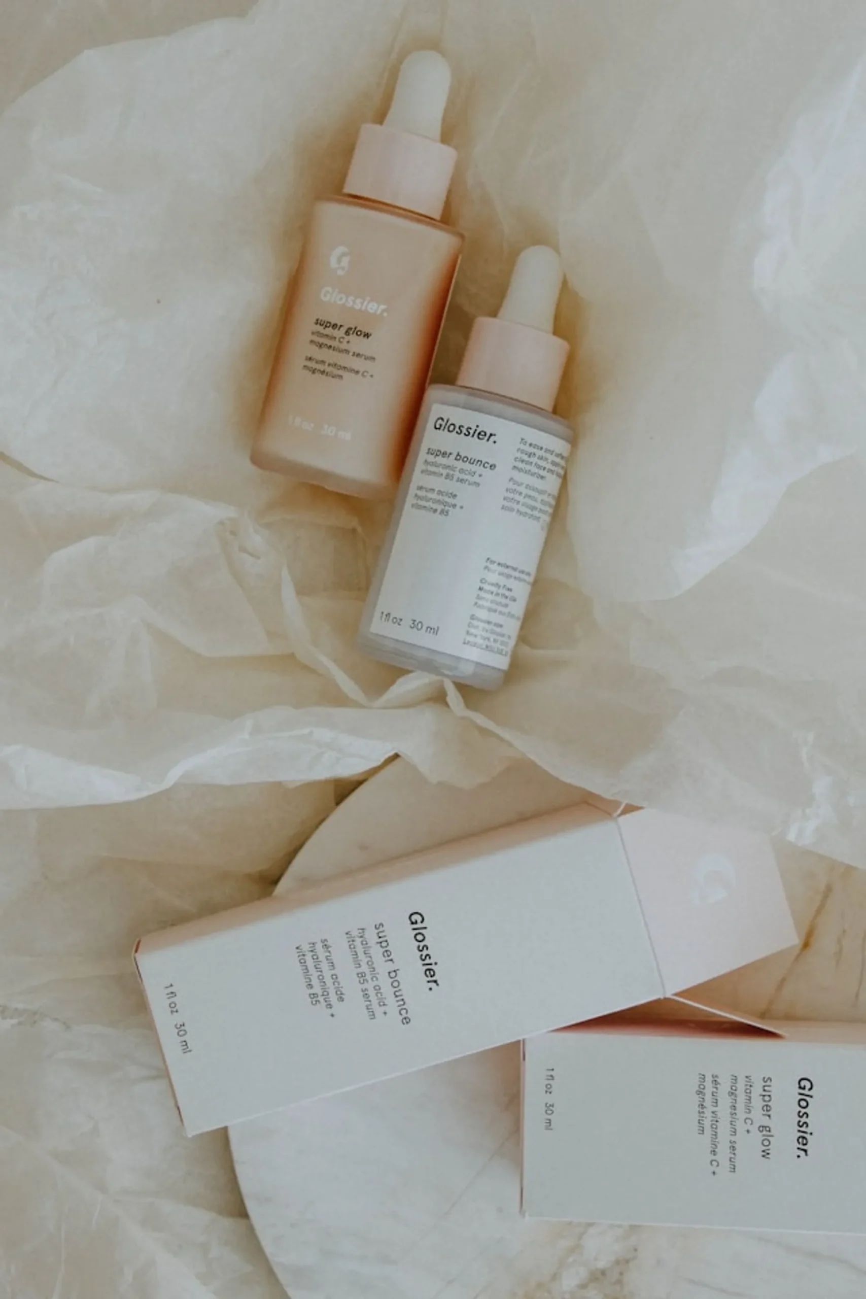 2 Glossier skincare for products in bottle , on top of a white woolen material, perfect for AM and PM skincare routine